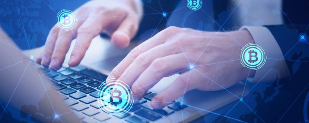 Hands typing on a keyboard with floating bitcoin symbols, representing the integration of blockchain technology into the digital world.